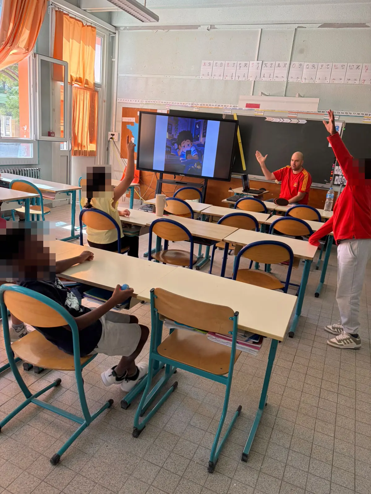 Un animateur échange avec la classe autour d'une illustration projetée à l'écran ; plusieurs élèves lèvent la main.