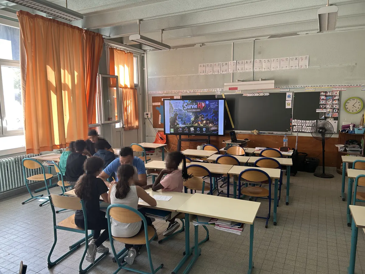 Des élèves travaillent en petits groupes autour d'un animateur, l'écran de la classe affichant un jeu.